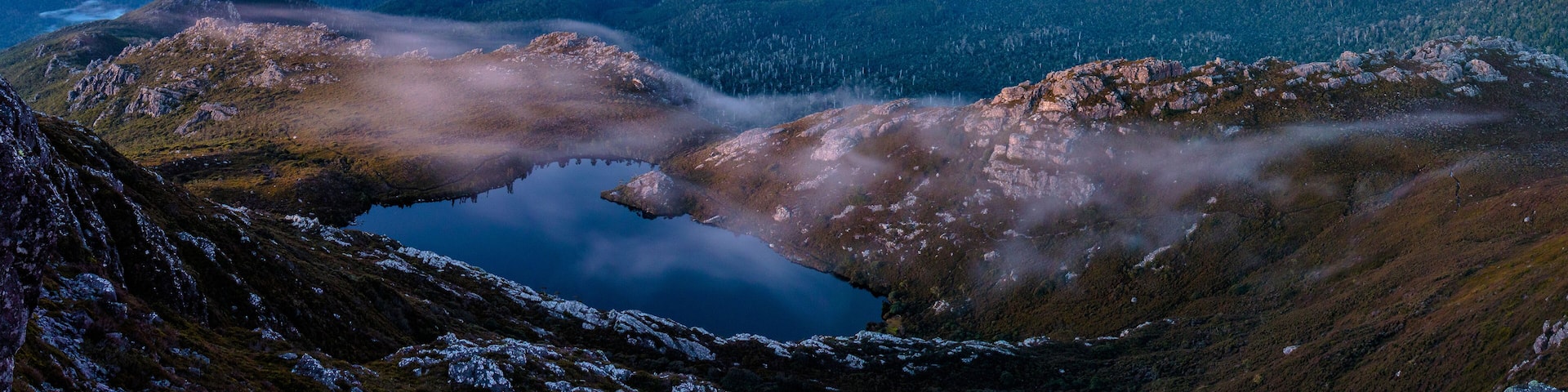 A mountainous landscape with a lake surrounded by rocky terrain and forested areas.