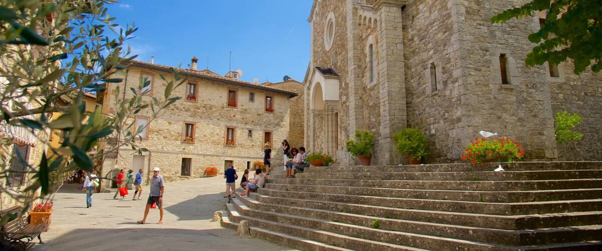 A stone building with a clock tower, steps leading up to it, and people walking around.