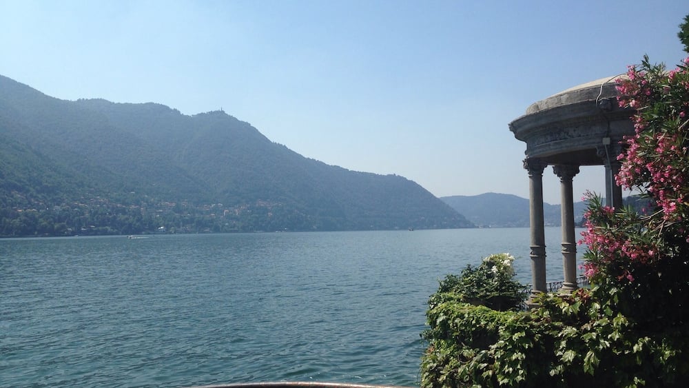 A lake with mountains in the background and a classical building with columns.
