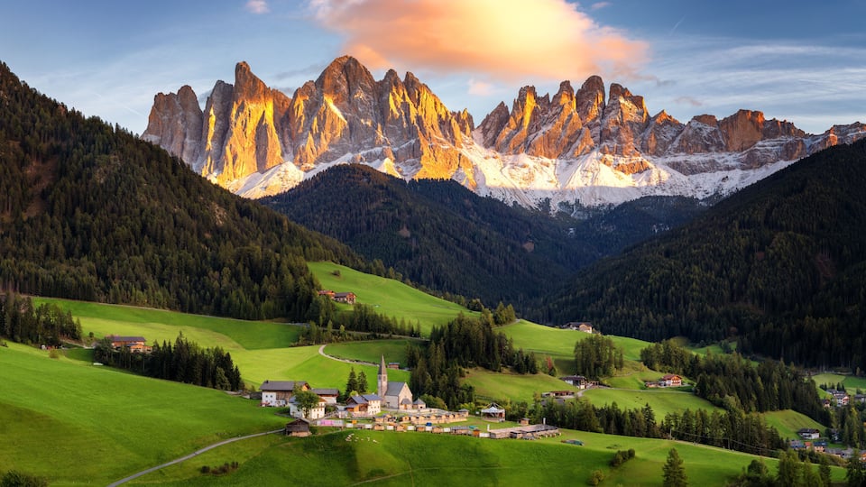 A mountainous landscape with a village nestled in the valley, surrounded by green fields and a prominent church.