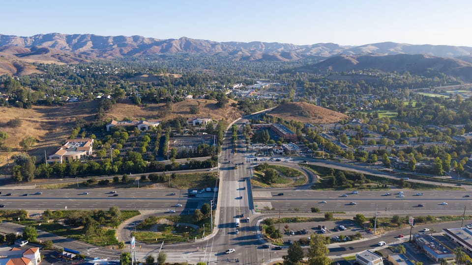 An aerial view of a highway interchange surrounded by mountains and residential areas.
