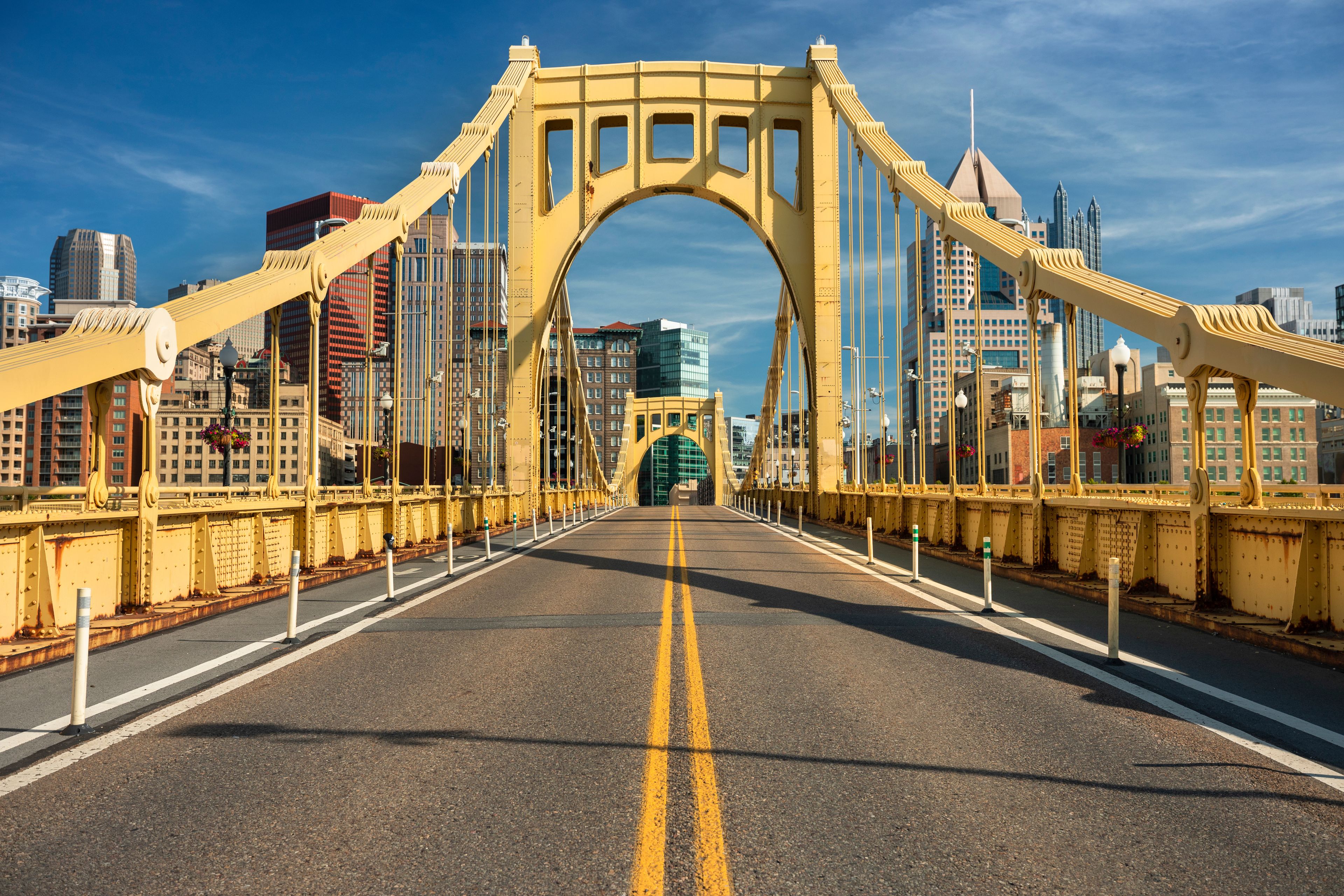 A yellow bridge with a road in the middle and buildings in the background.