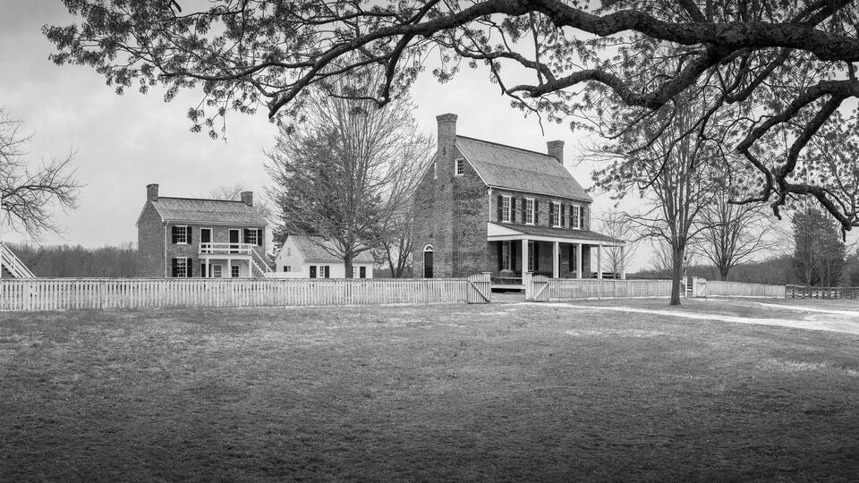 A large, historic house with a prominent front porch and a large tree in the foreground.