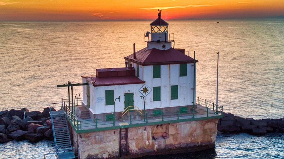 A lighthouse on a rocky outcrop with a sunset in the background.