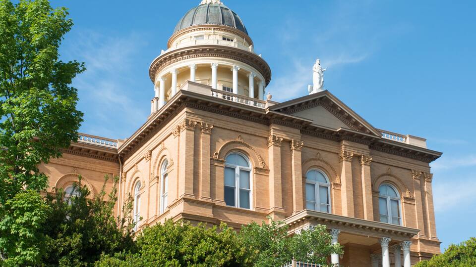 A large, historic building with a dome and columns, surrounded by lush greenery.