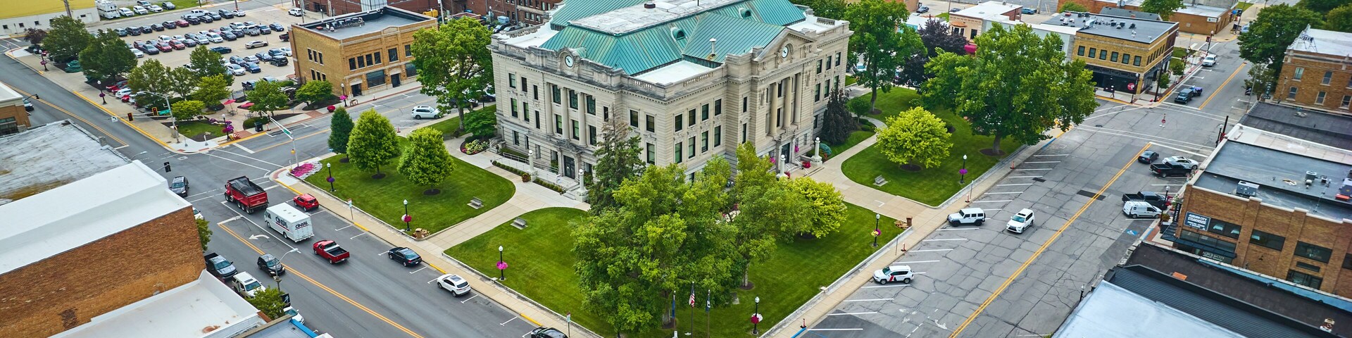 An aerial view of a town with a prominent historic building, a central intersection, and surrounding greenery.