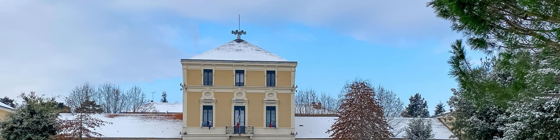 A snow-covered courtyard with a yellow building featuring a central tower and multiple windows.
