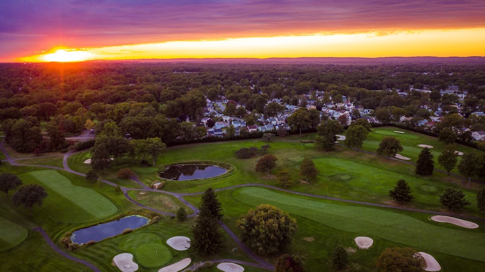 A golf course with sand bunkers, water hazards, and a sunset in the background.