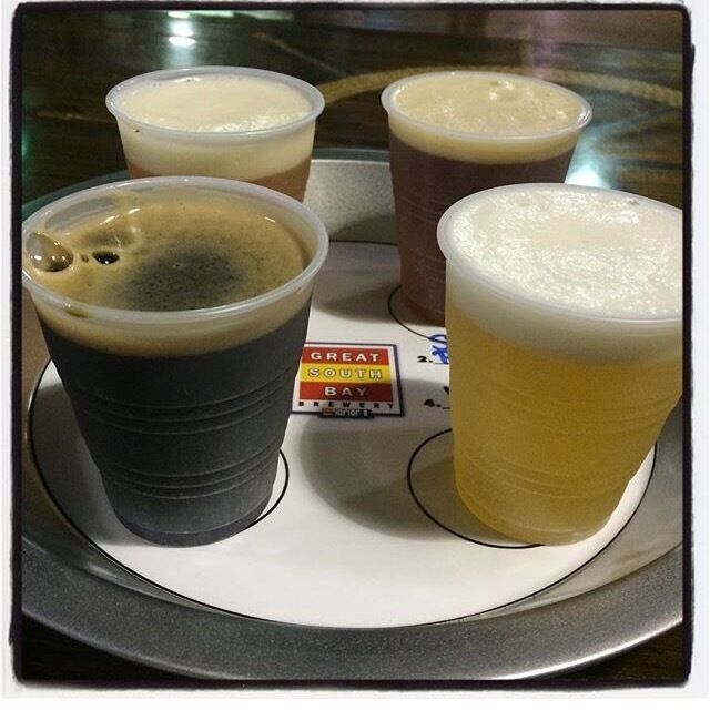 Four plastic cups of different beverages on a tray with a label that reads "Great South Bay."