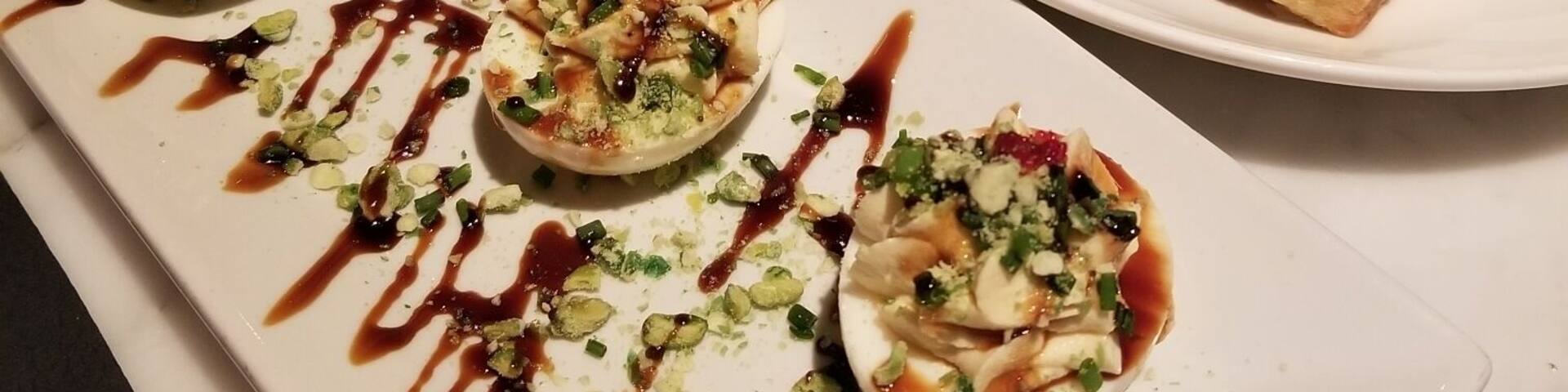 A dessert plate with three small pastries topped with green onions and drizzled with sauce.