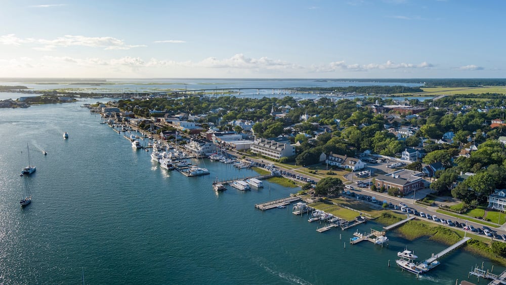 A coastal town with a marina, boats, and a bridge in the distance.