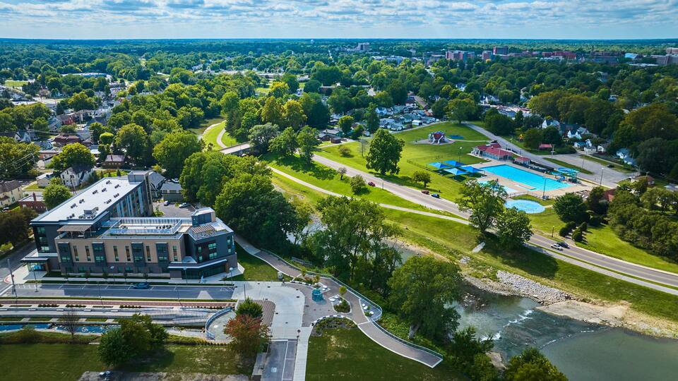 An aerial view of a university campus with a swimming pool, green spaces, and a river.