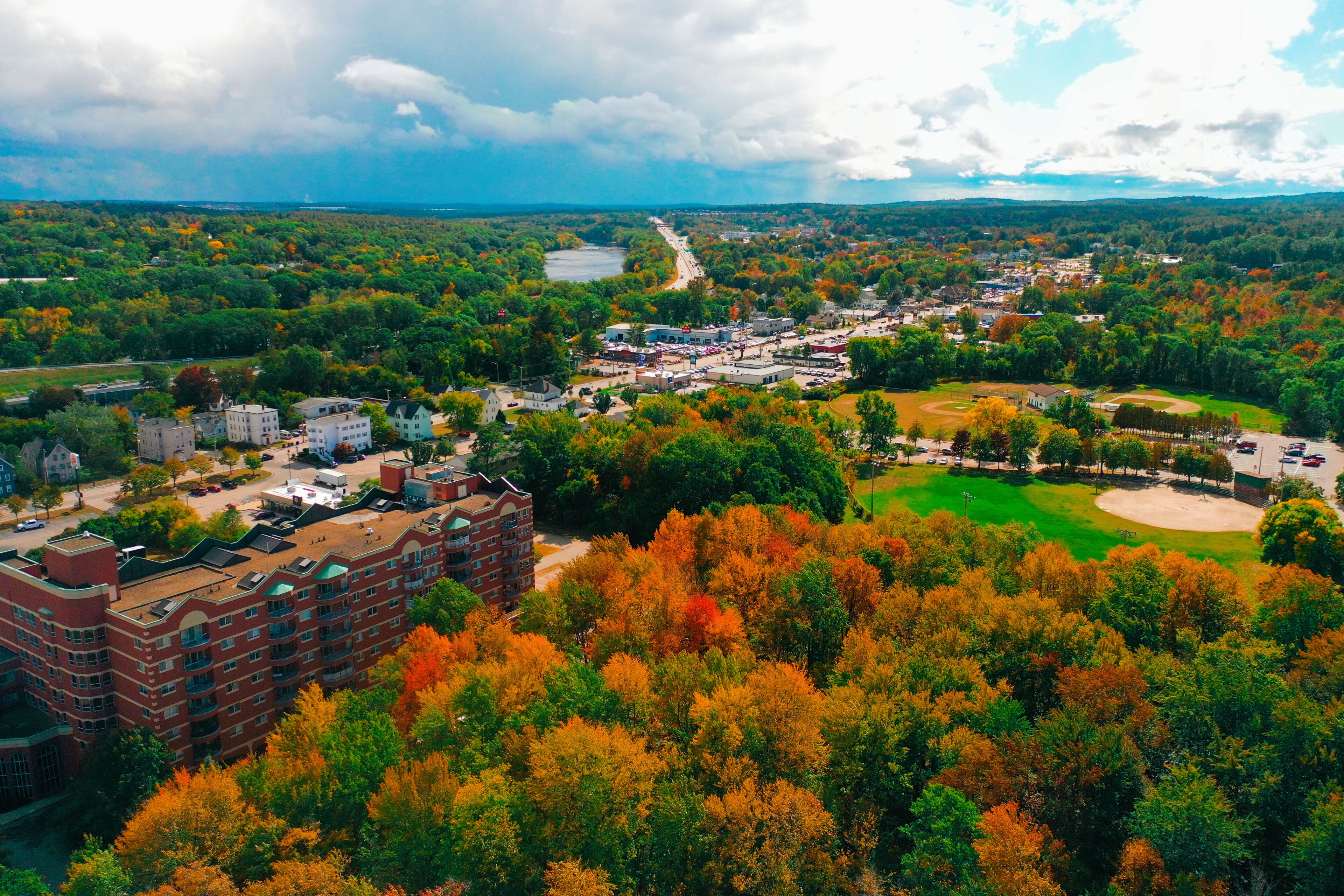 An aerial view of a town with autumn foliage, a river, and a baseball field.