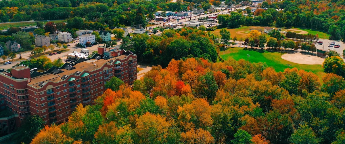 An aerial view of a town with autumn foliage, a river, and a baseball field.