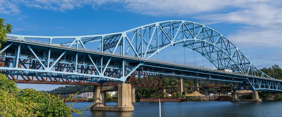 A large blue steel bridge spanning a river with a clear sky above.