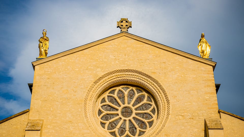 A church with a large circular window and two golden statues on the roof.