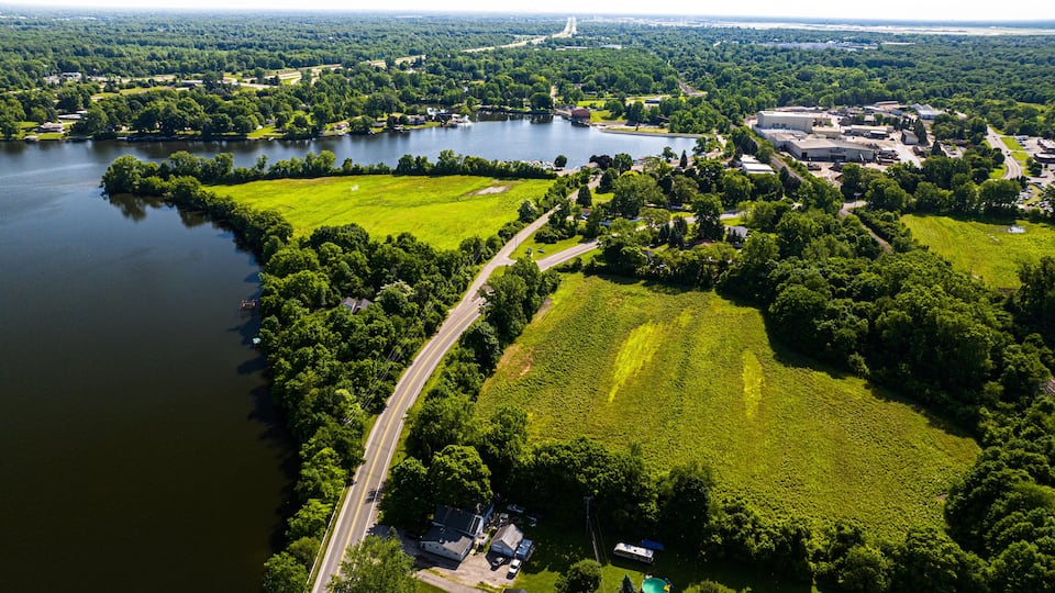 An aerial view of a lakeside area with a road, green fields, and buildings.