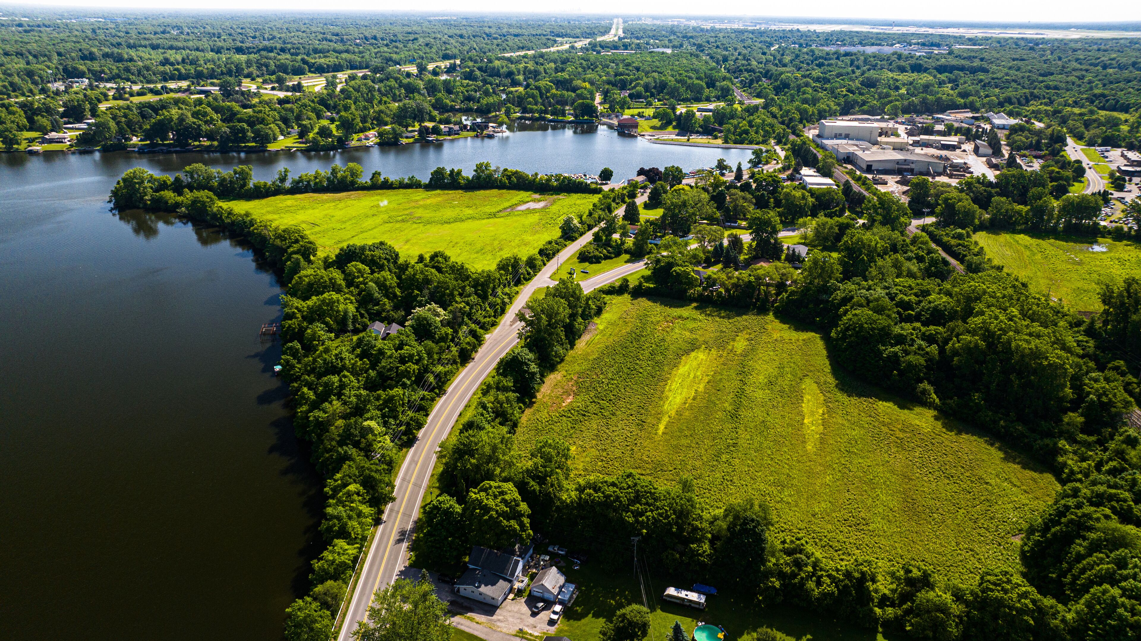 An aerial view of a lakeside area with a road, green fields, and buildings.