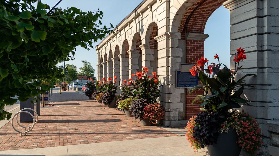 A brick pathway leading to a stone archway with red flowers in planters.