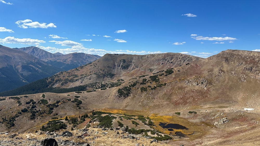 A mountainous landscape with rocky terrain, sparse vegetation, and a clear blue sky.