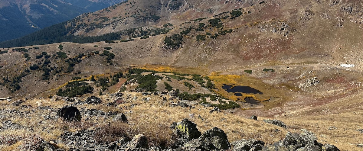 A mountainous landscape with rocky terrain, sparse vegetation, and a clear blue sky.