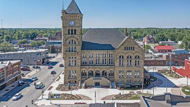 A historic building with a clock tower, surrounded by a town square with roads and other buildings.