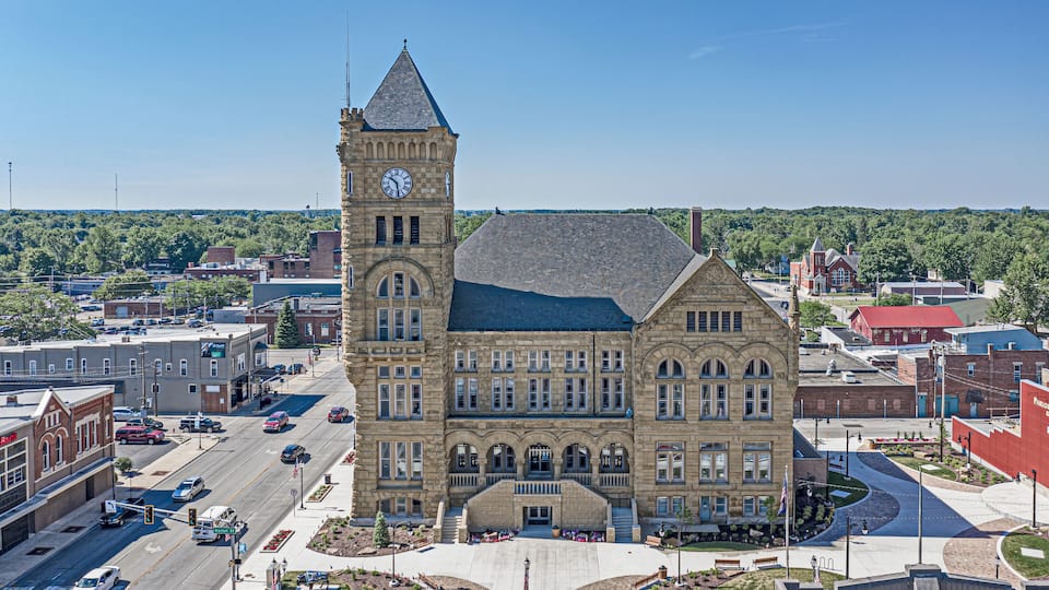 A historic building with a clock tower, surrounded by a town square with roads and other buildings.