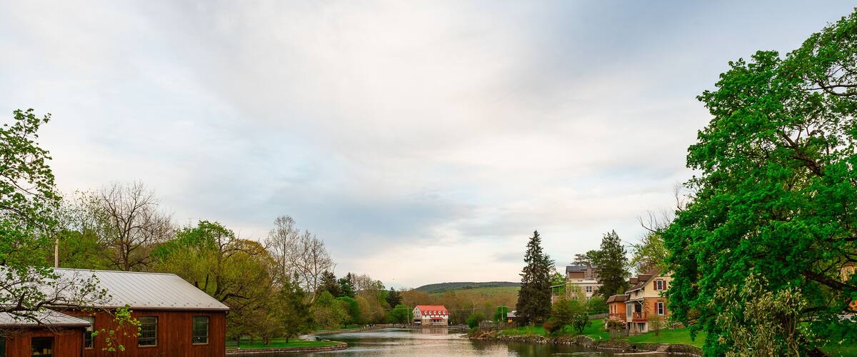 A river with ducks, a wooden building, and a house with a red roof.