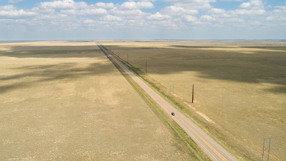 A long straight road in a flat, open landscape with sparse vegetation and a clear sky.
