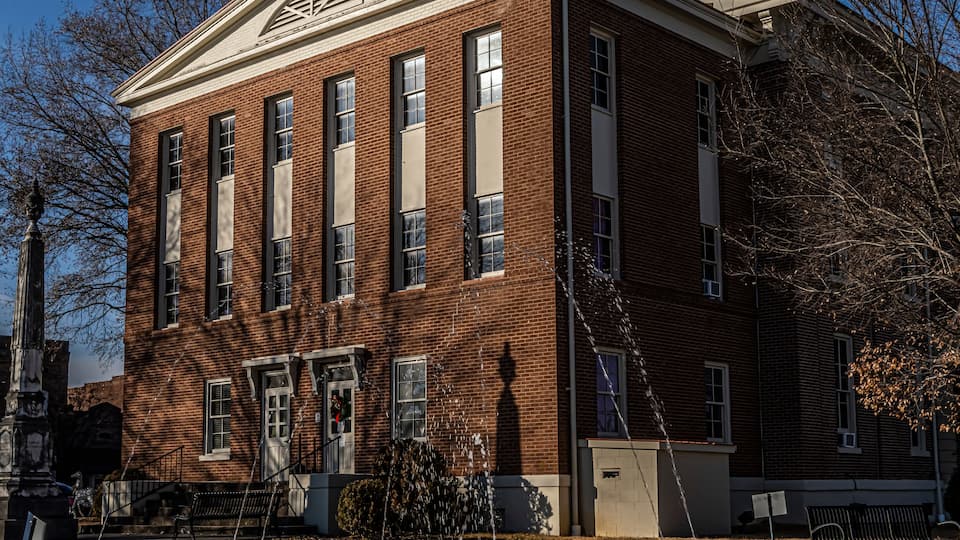 A red brick building with a dome and columns, a fountain, and trees.