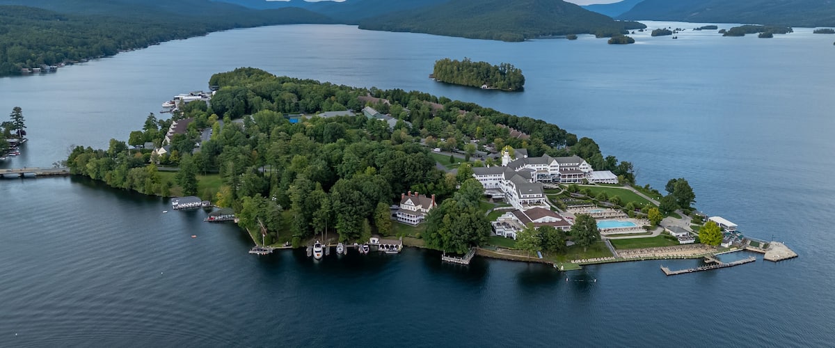 An aerial view of a small island with dense forests, a large white mansion, and a dock with boats.