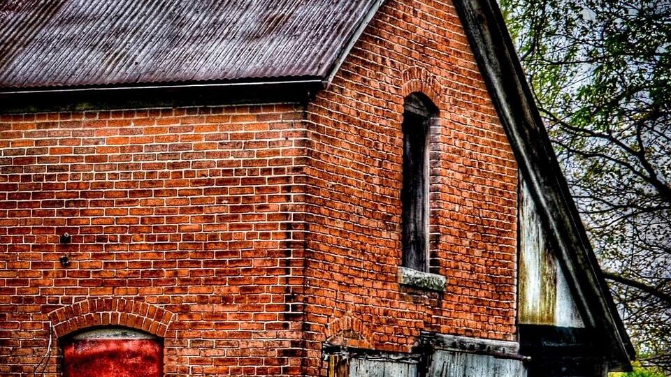 A rustic brick building with a red door and a wooden fence.
