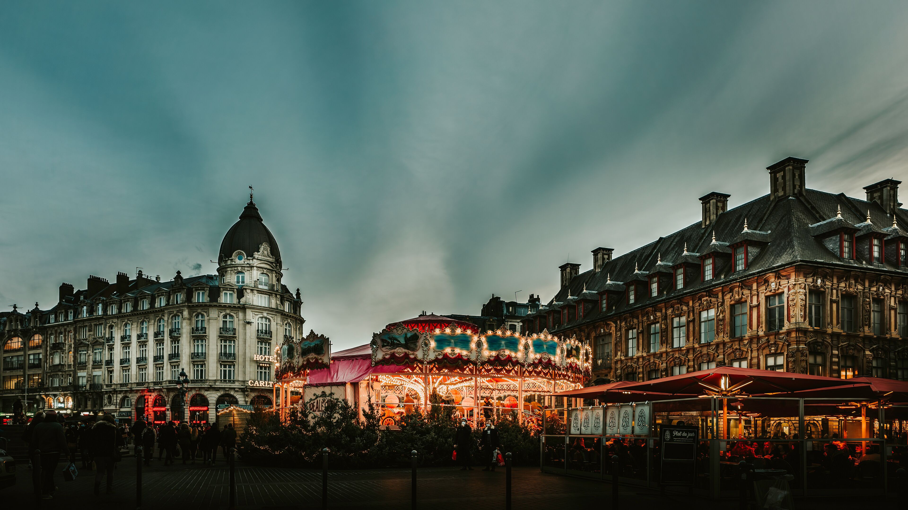 A historic European square with ornate buildings, a prominent dome, and a brightly lit carousel.