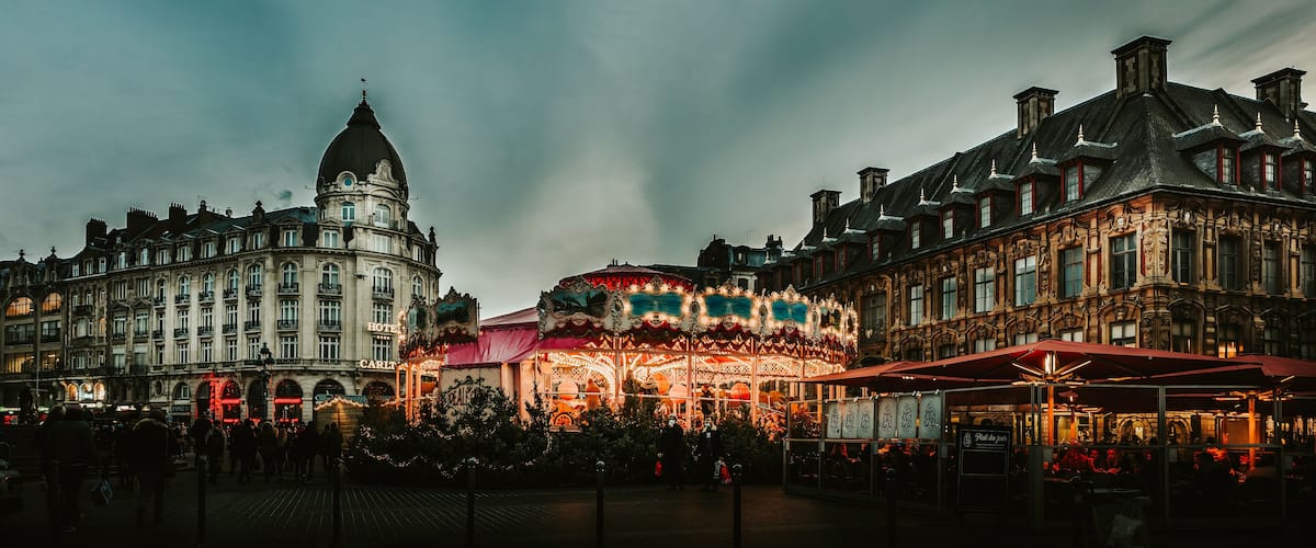 A historic European square with ornate buildings, a prominent dome, and a brightly lit carousel.