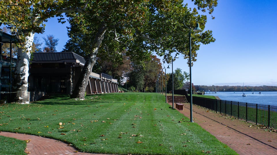 A park with a river, a bridge, and a building with a black roof.