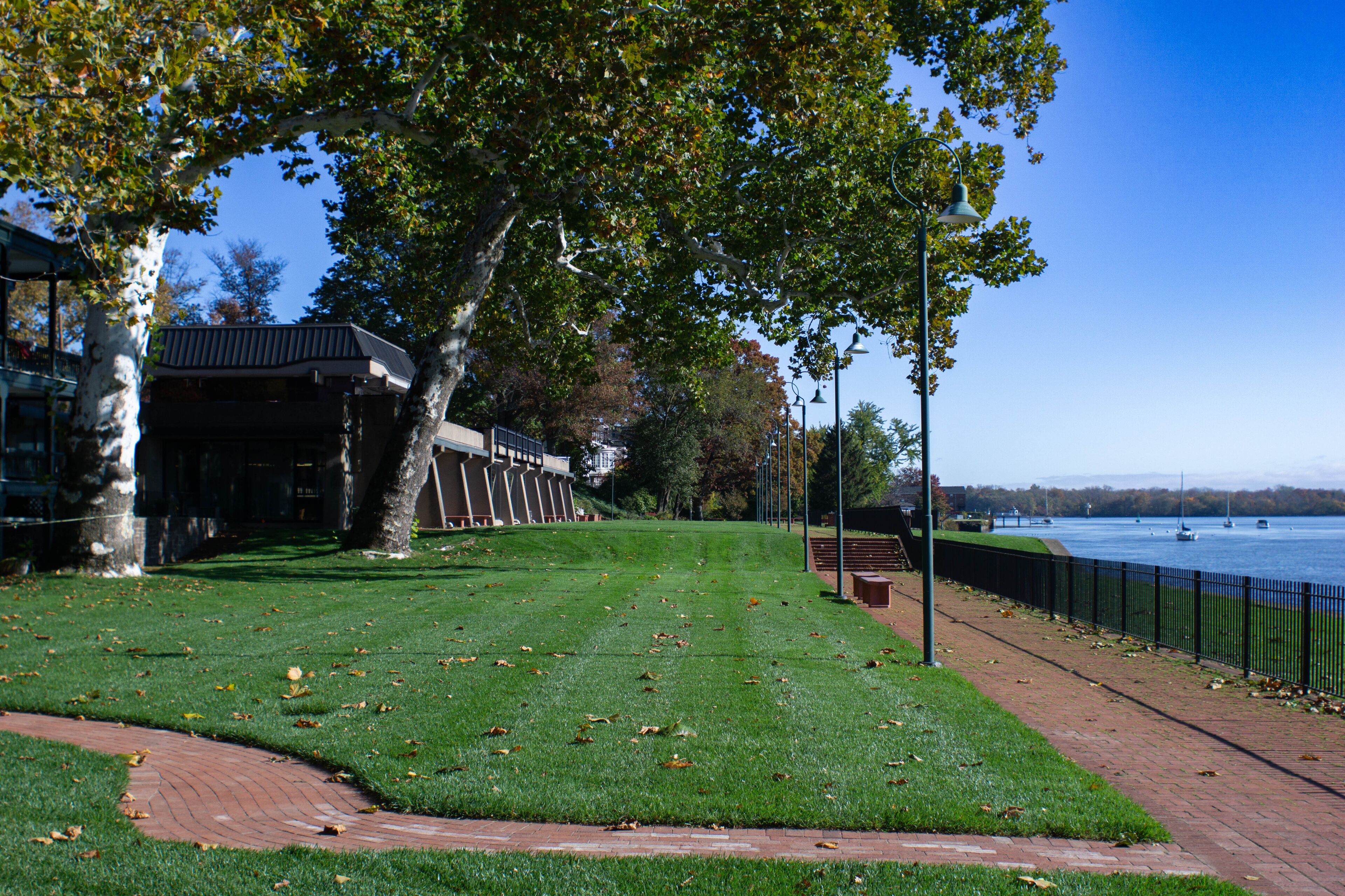 A park with a river, a bridge, and a building with a black roof.