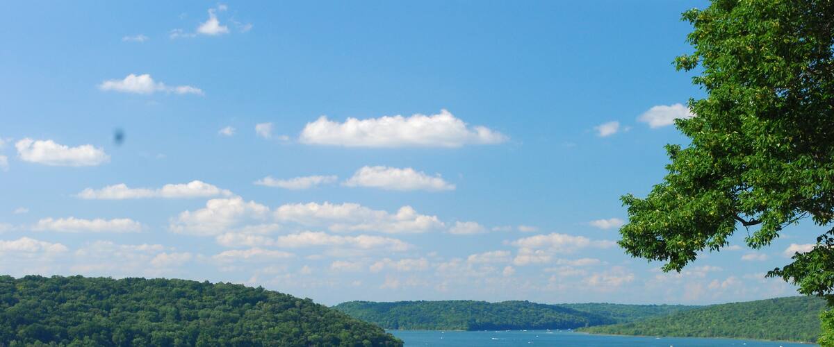 A lake surrounded by green hills and trees under a clear sky.