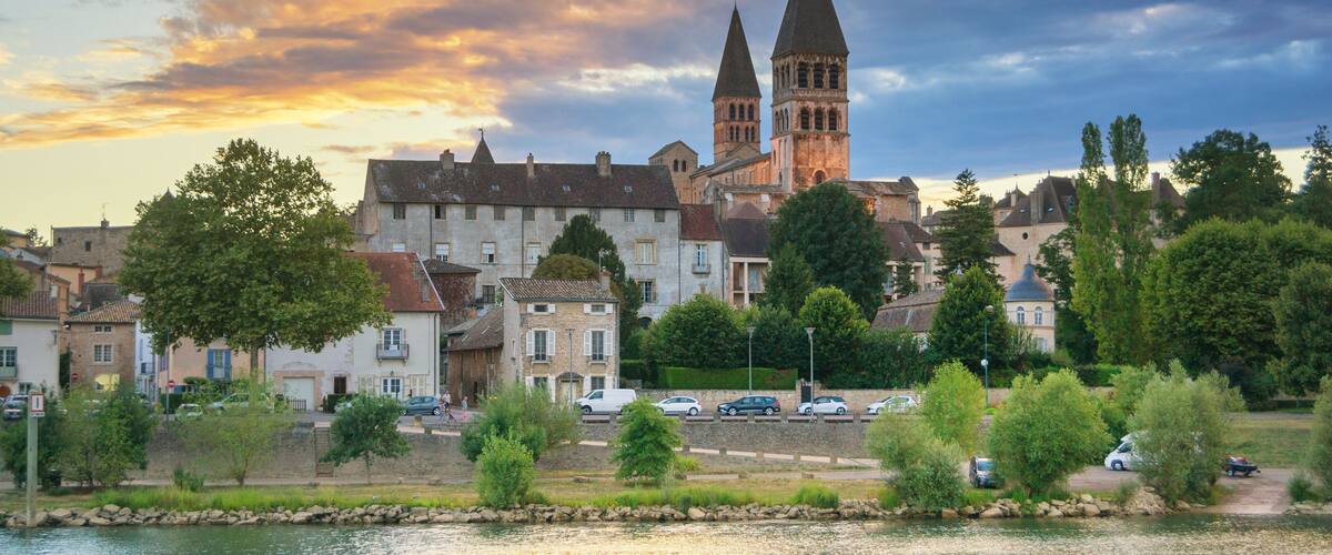 A riverside town with historic buildings and a prominent church with two towers.
