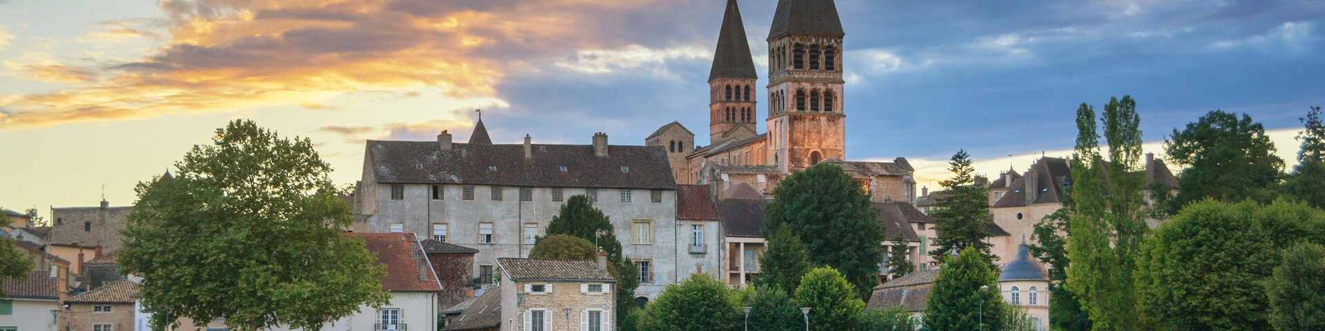 A riverside town with historic buildings and a prominent church with two towers.