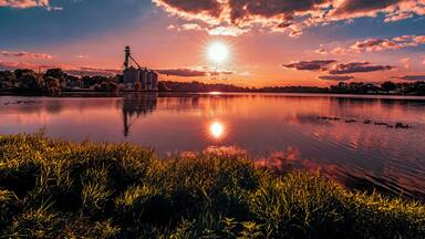 On the grassy shore of a rural southern Wisconsin lake with a view of the sun setting over the silhouettes in the distance at sunset in Burlington, Wisconsin USA.