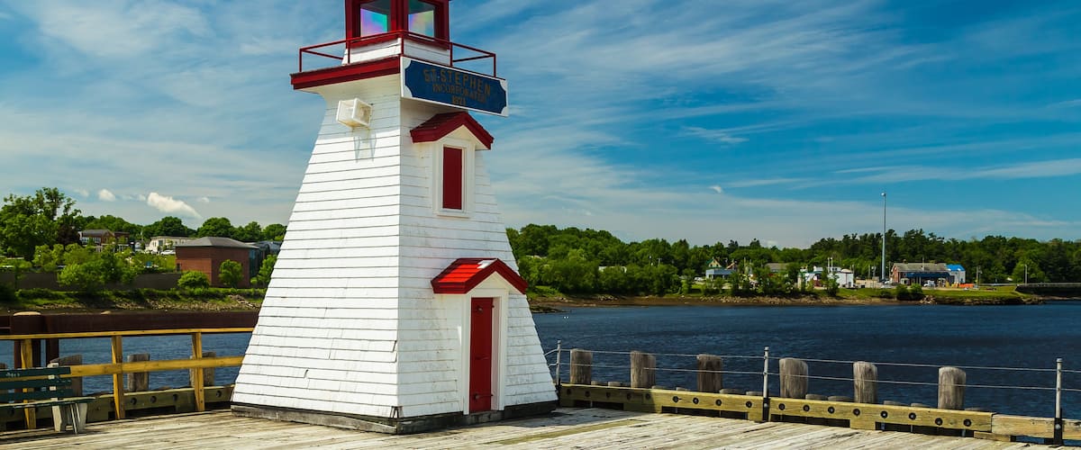 A white lighthouse with a red roof and a sign reading "Ste. Stephen Incorporated 1871" on a wooden pier.