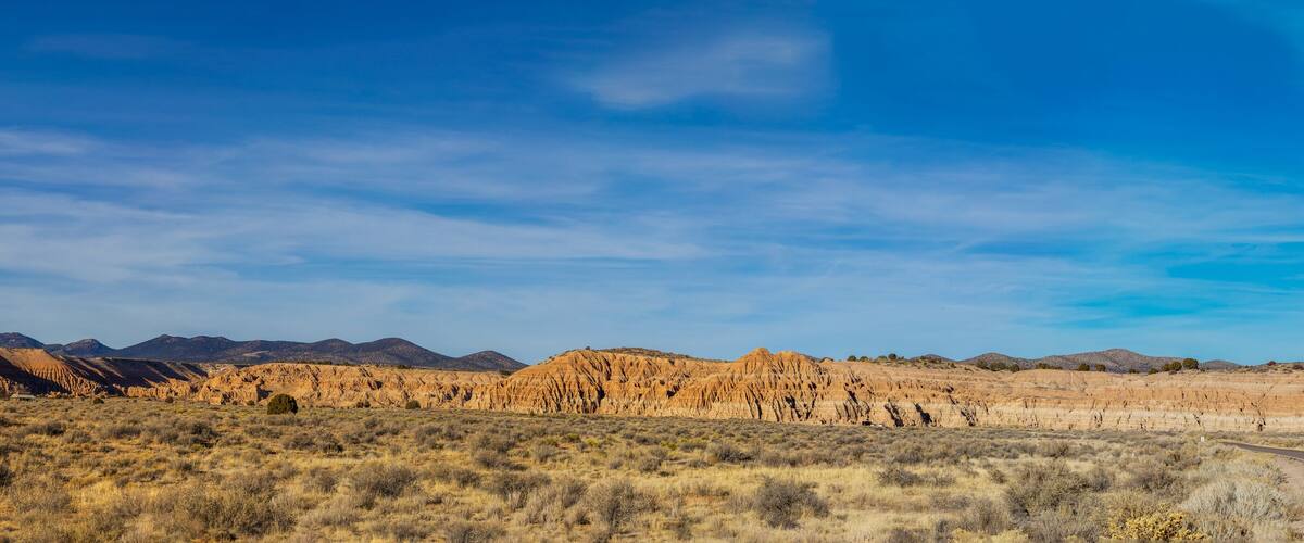 A desert landscape with rolling hills and mountains in the background under a clear blue sky.