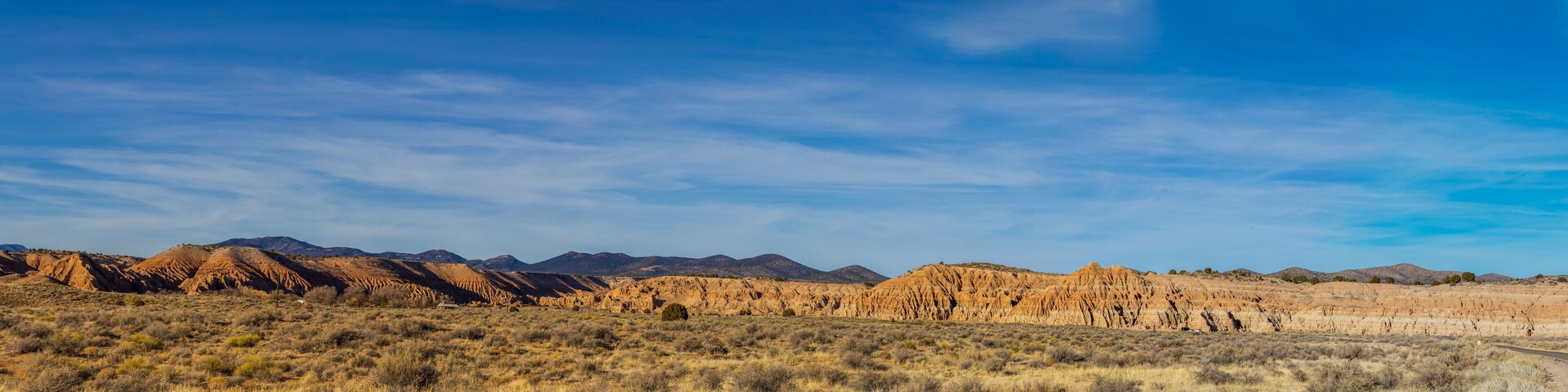 A desert landscape with rolling hills and mountains in the background under a clear blue sky.