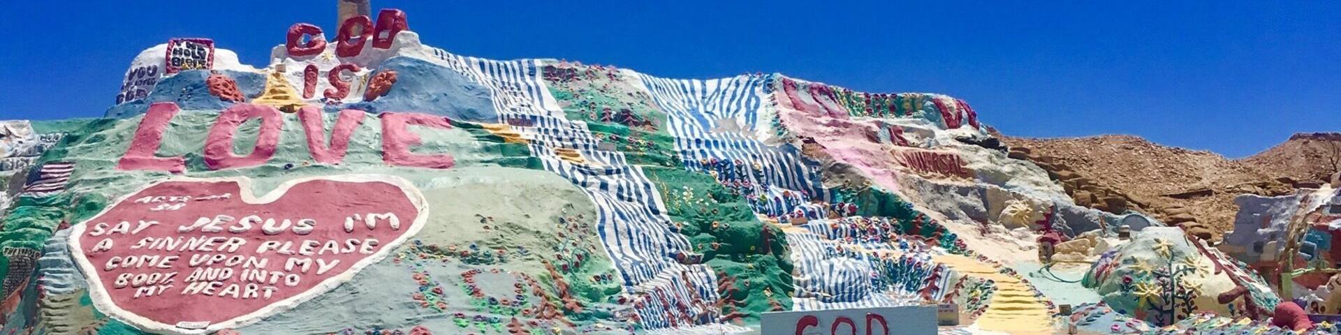 A colorful hill with a cross and a heart-shaped sign with religious messages.