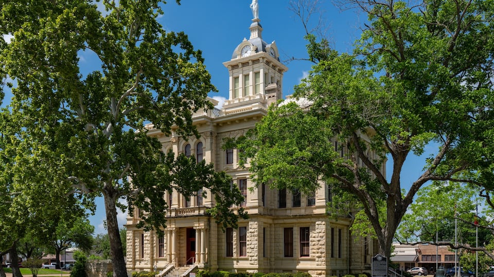 A historic building with a clock tower, surrounded by lush green trees.