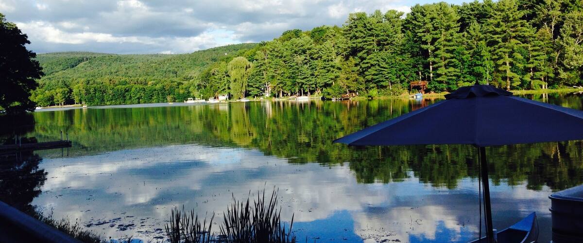 A calm lake with reflections of the sky and trees, surrounded by lush greenery and hills.
