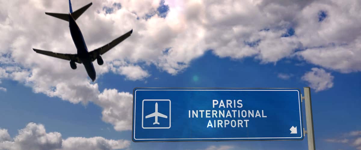 An airplane flying against a partly cloudy sky with a sign for Paris International Airport.