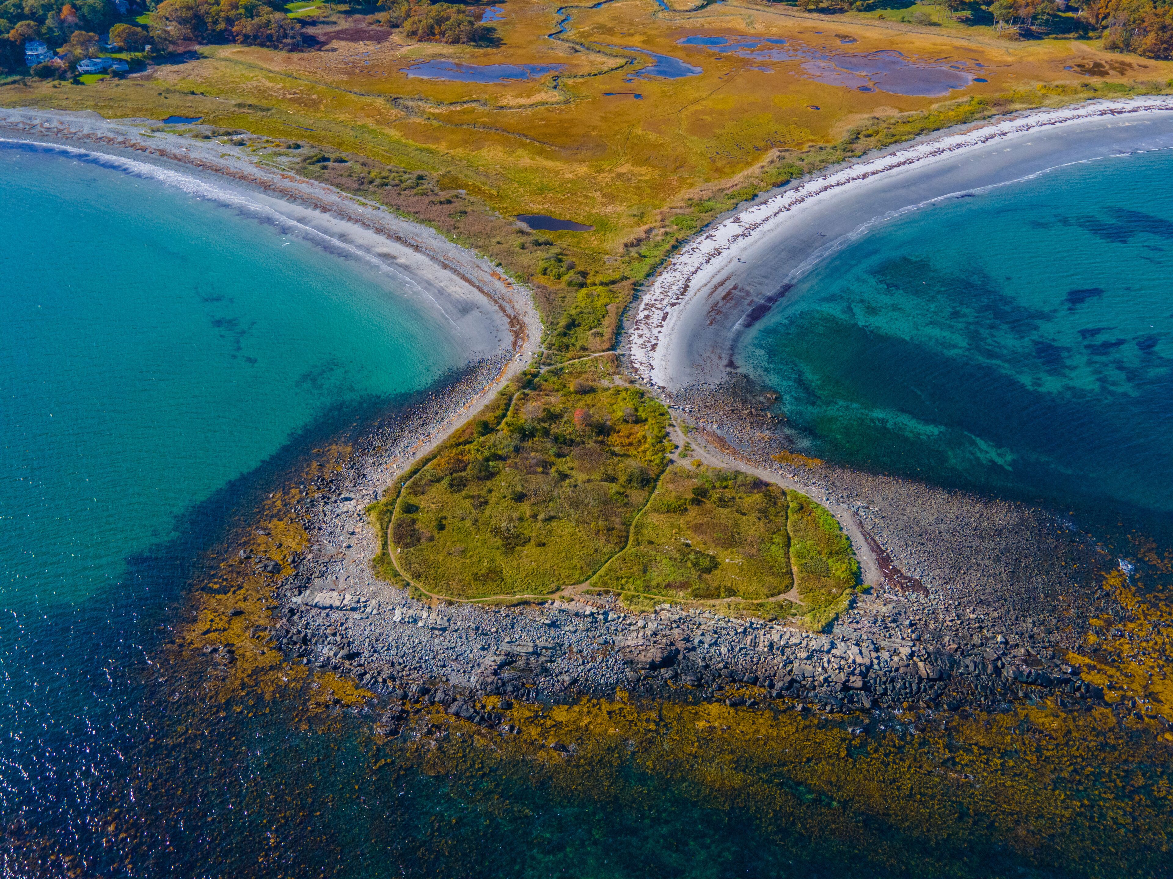 Un paisaje costero donde dos masas de agua distintas convergen en un punto central, rodeado de costas rocosas y zonas con vegetación.