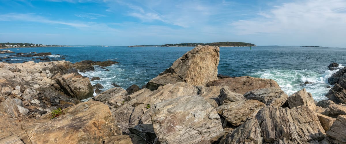 A rocky coastline with waves crashing against the rocks and a distant island.