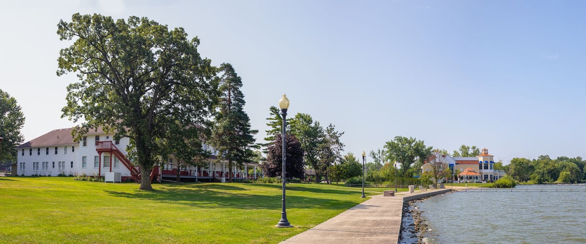 A waterfront with a grassy area, a row of trees, and a building with a red staircase.